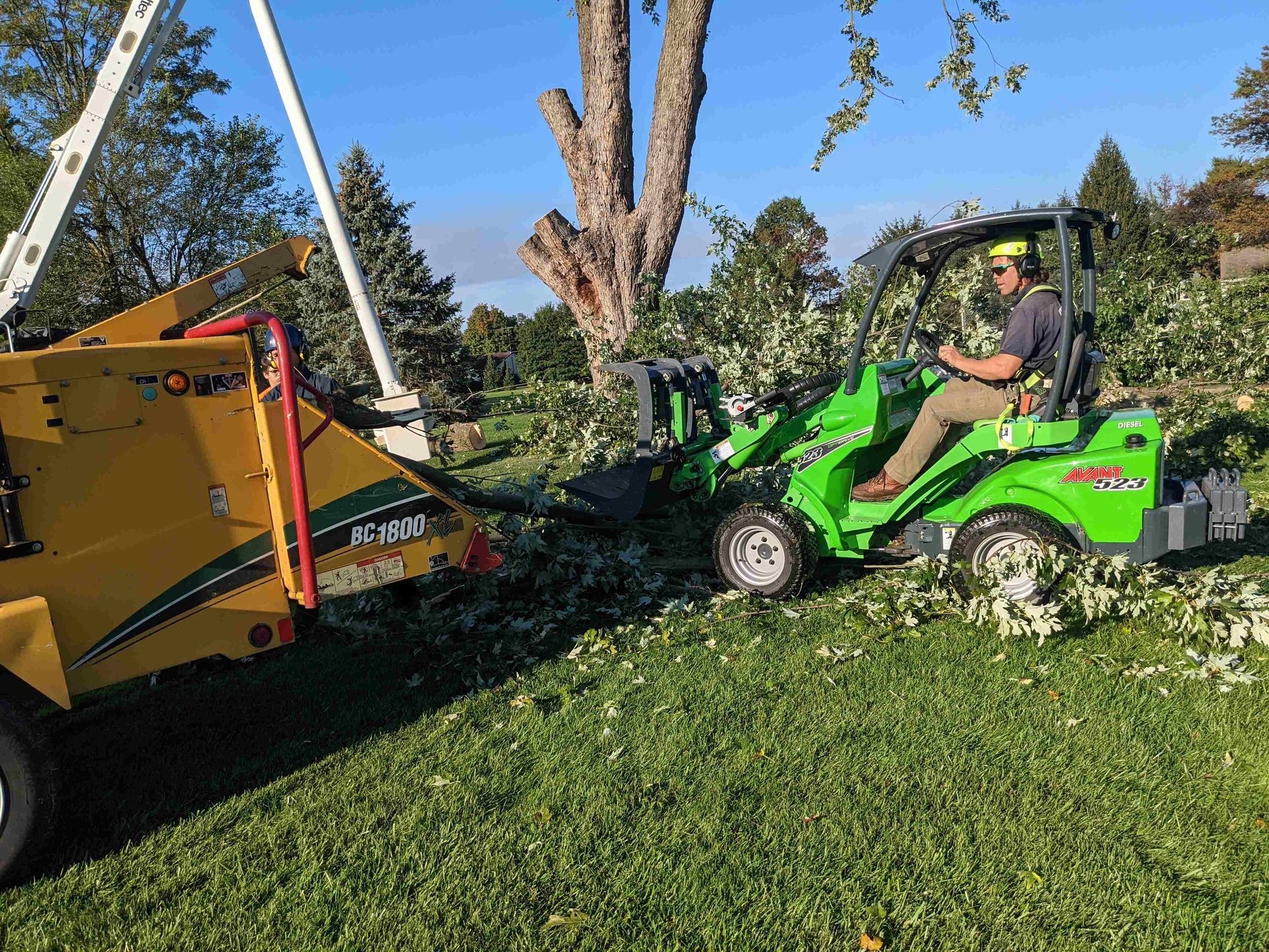 A man is driving a green tractor next to a tree chipper.