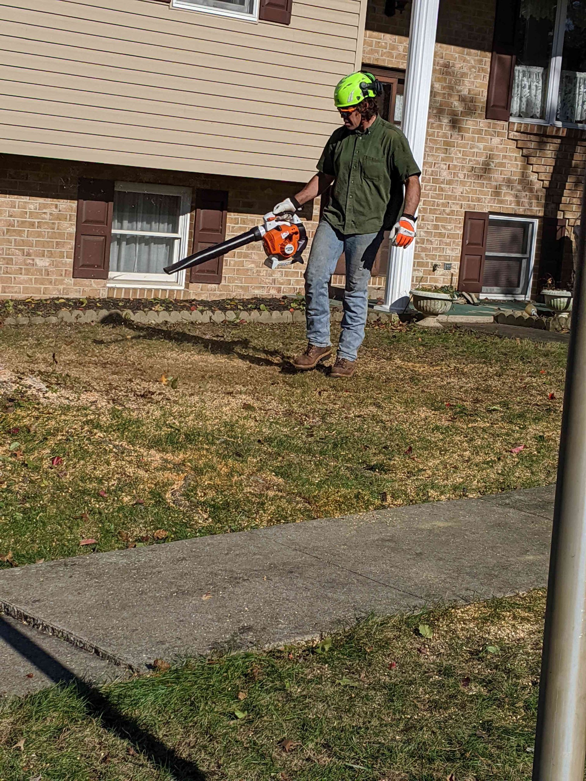 A man is blowing grass in front of a house with a blower.