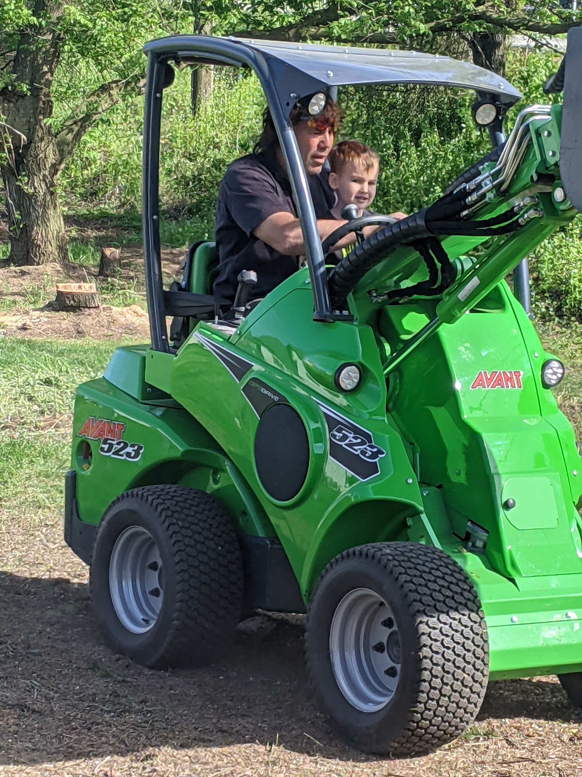 A man and a child are riding a green tractor.