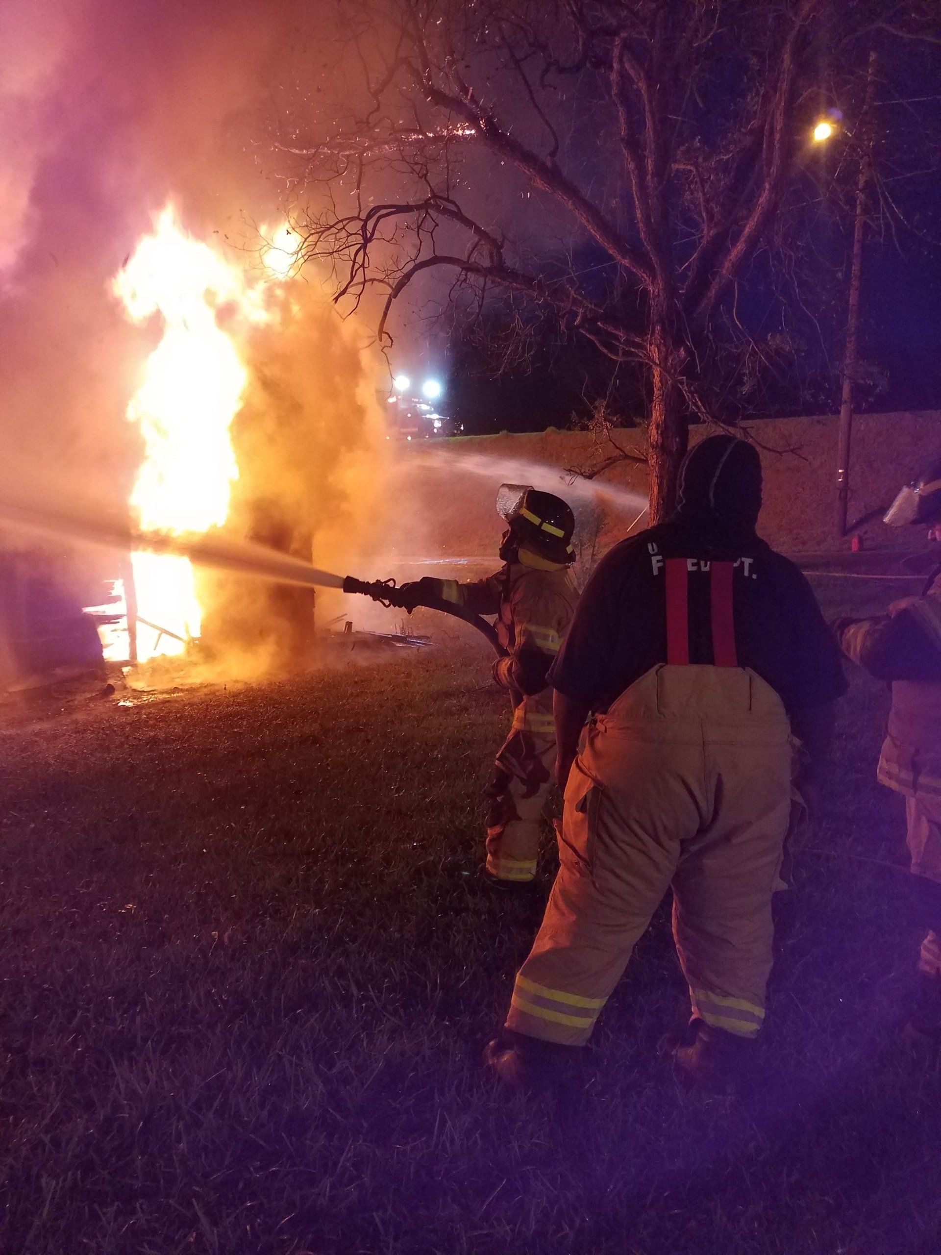 Two firefighters are spraying water on a fire at night.