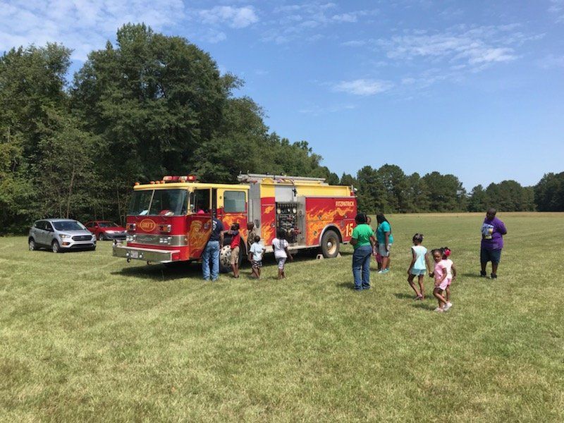 A group of people are standing around a fire truck in a field.