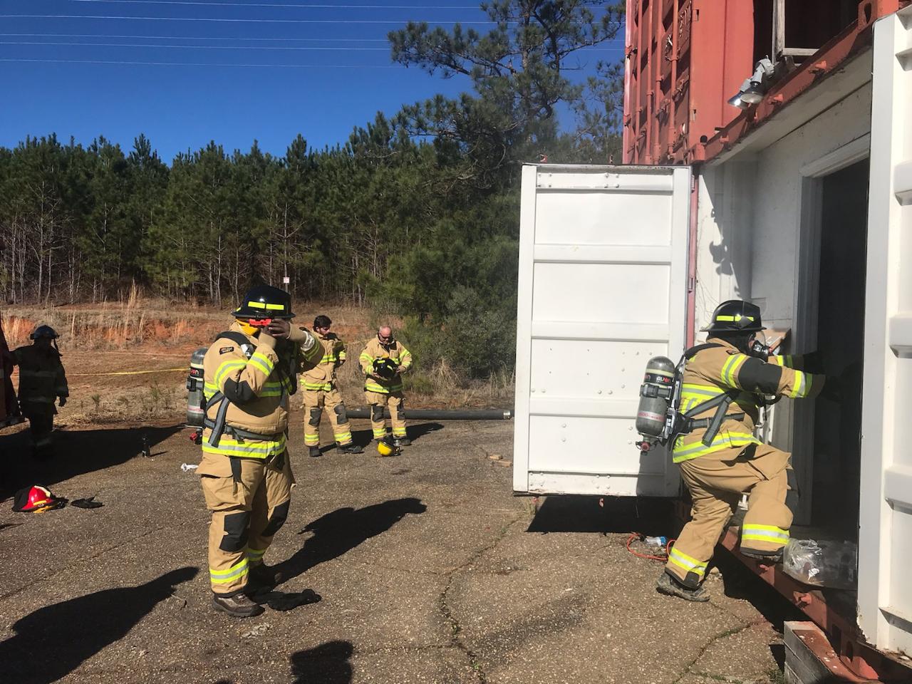 A group of firefighters are standing next to a shipping container.