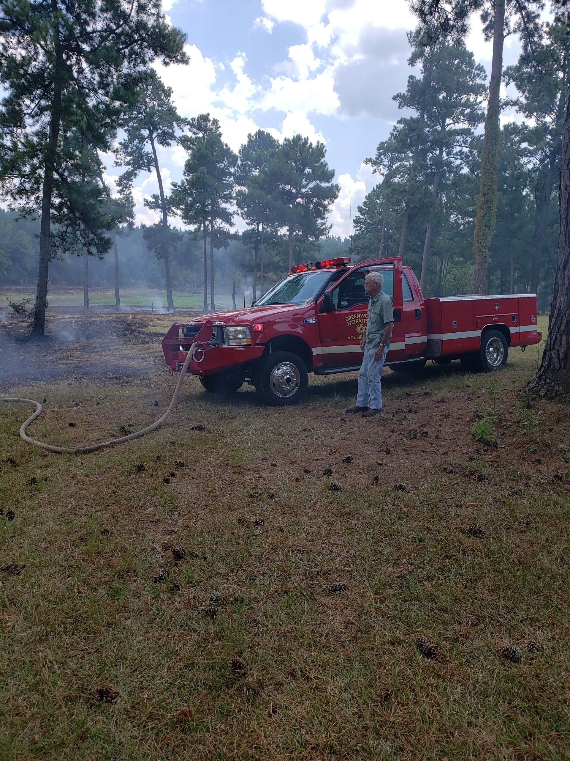 A man is standing next to a red truck in a field.