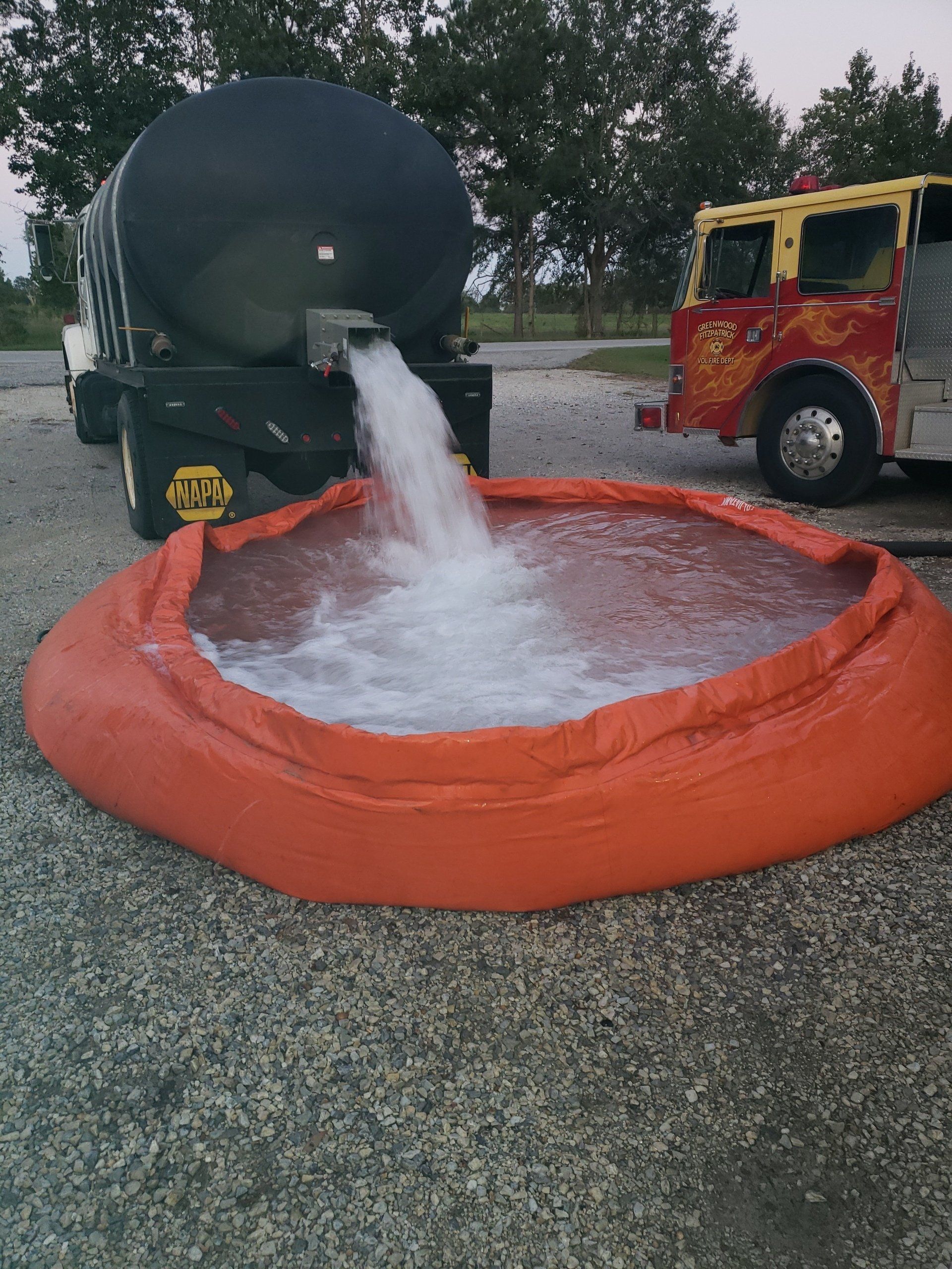 A fire truck is pouring water into an orange container