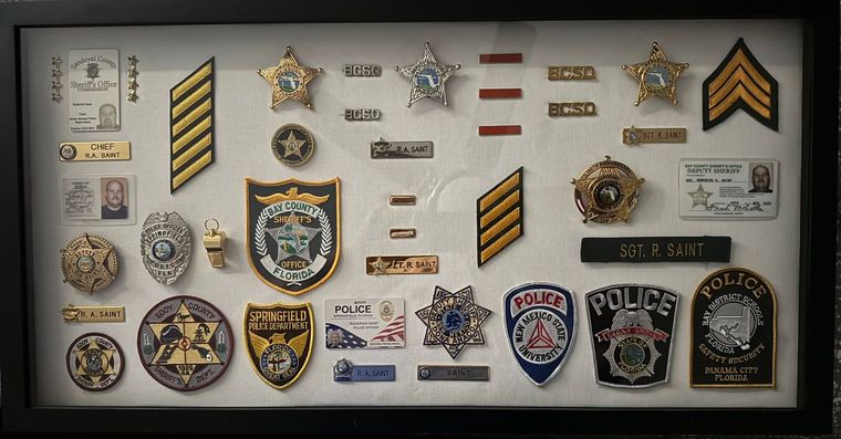 Framed display of police badges, patches, rank insignia, and emblems on a white background