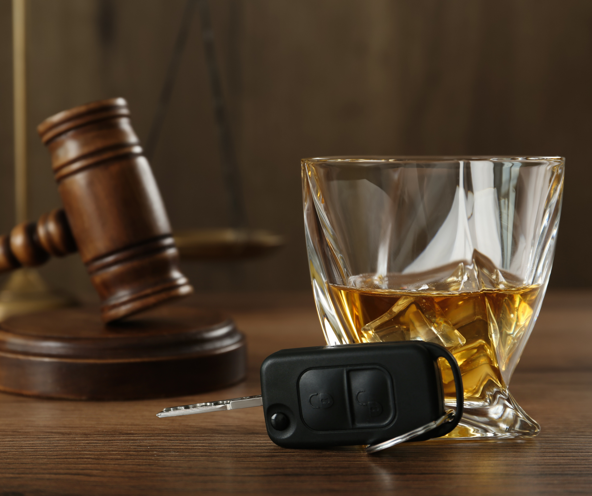 A glass of whiskey , a car key , and a judge 's gavel are on a wooden table.