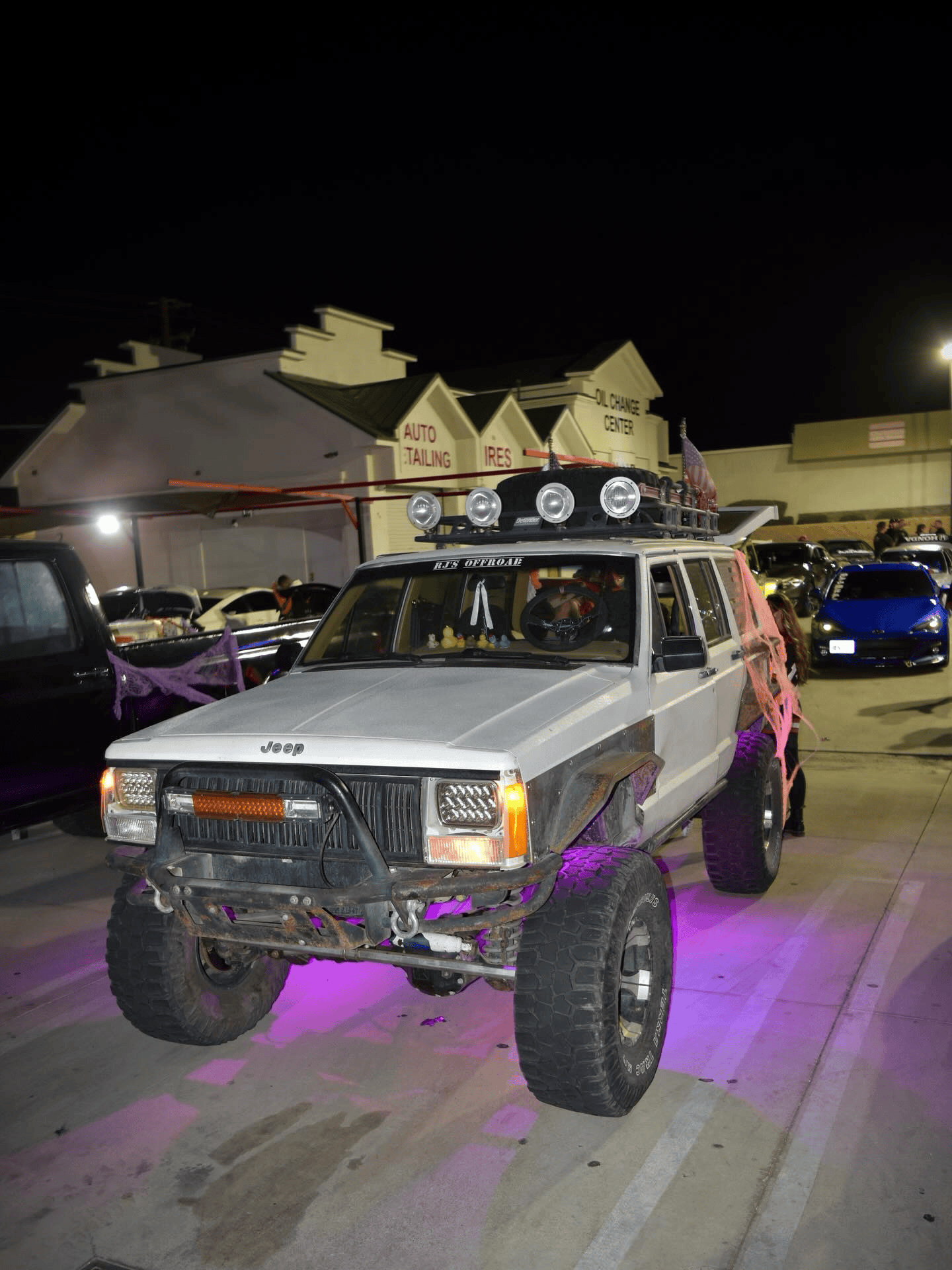 White lifted Jeep with roof lights and purple underglow parked at night in a lot