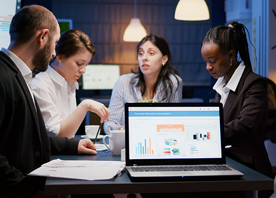 A group of people are sitting around a table looking at a laptop.