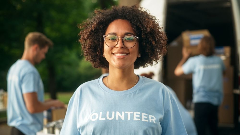 A woman wearing a blue volunteer shirt is smiling in front of a van.