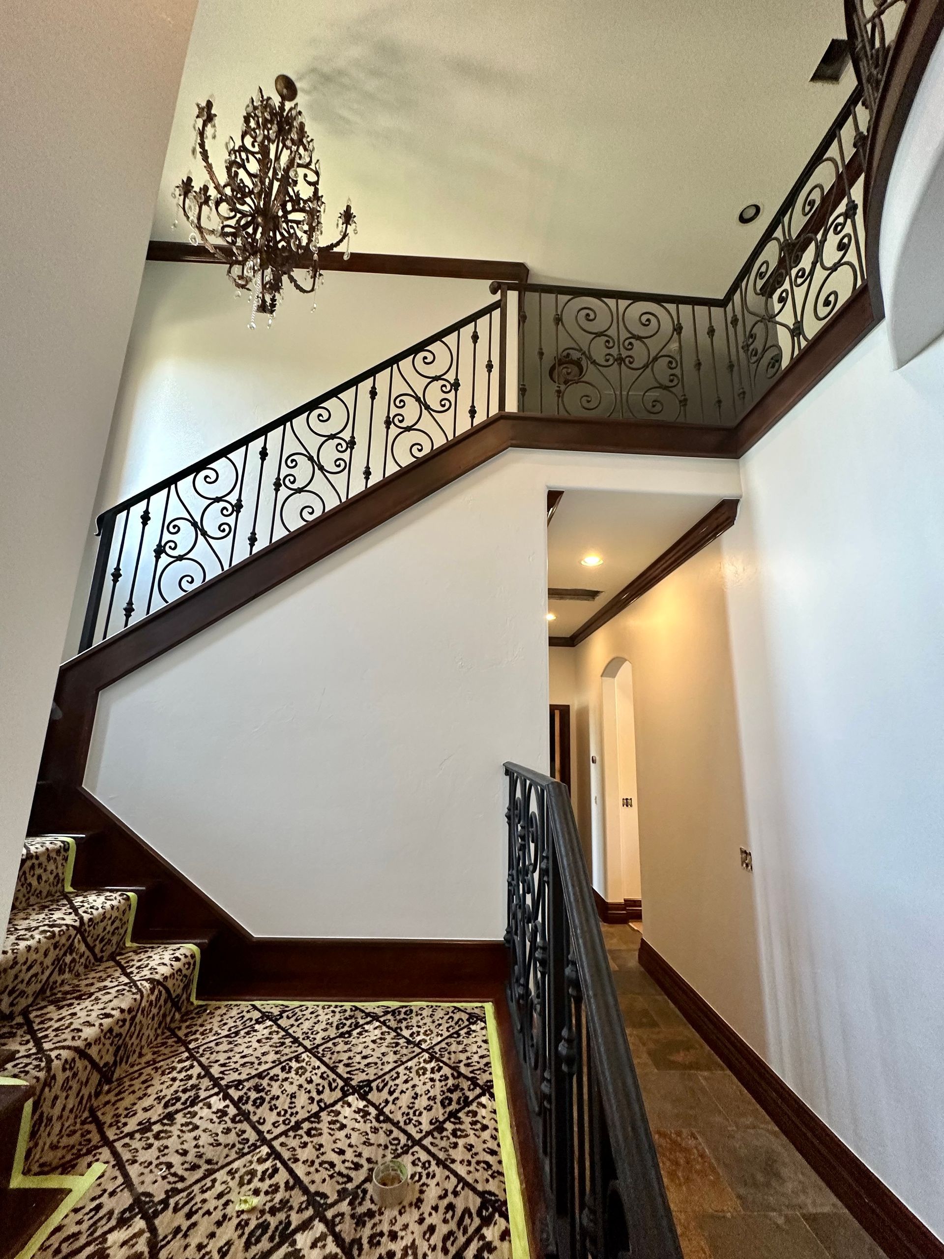 A staircase with a wrought iron railing and a chandelier hanging from the ceiling