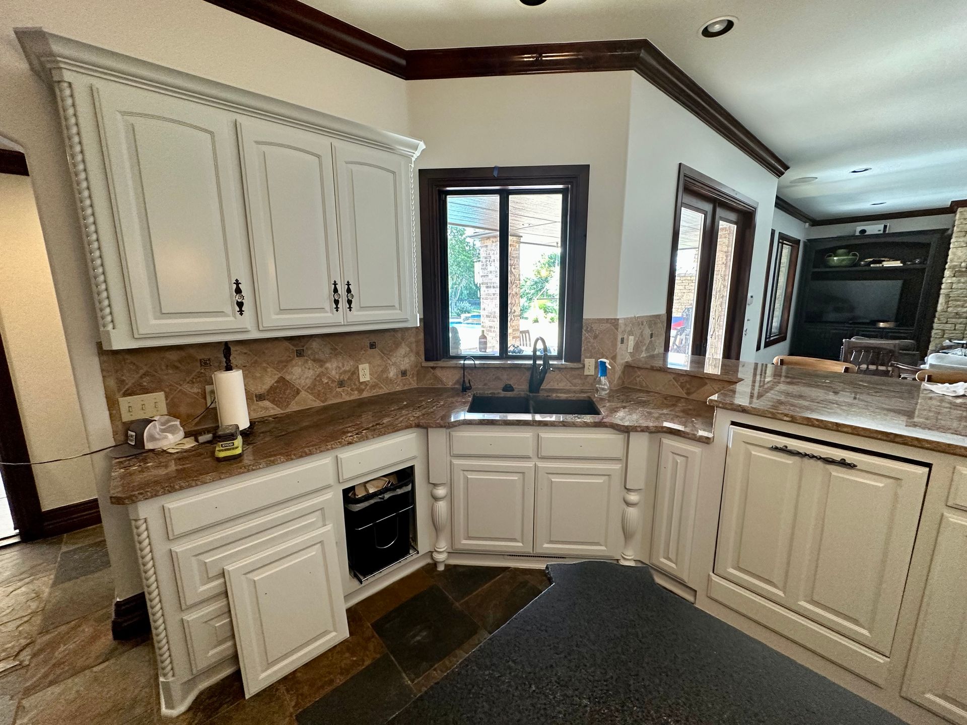 A kitchen with white cabinets , granite counter tops , a sink and a window.