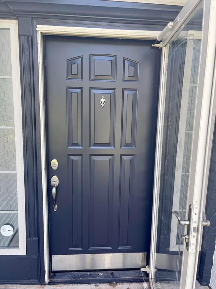 A black door with a stainless steel trim is open to a house.