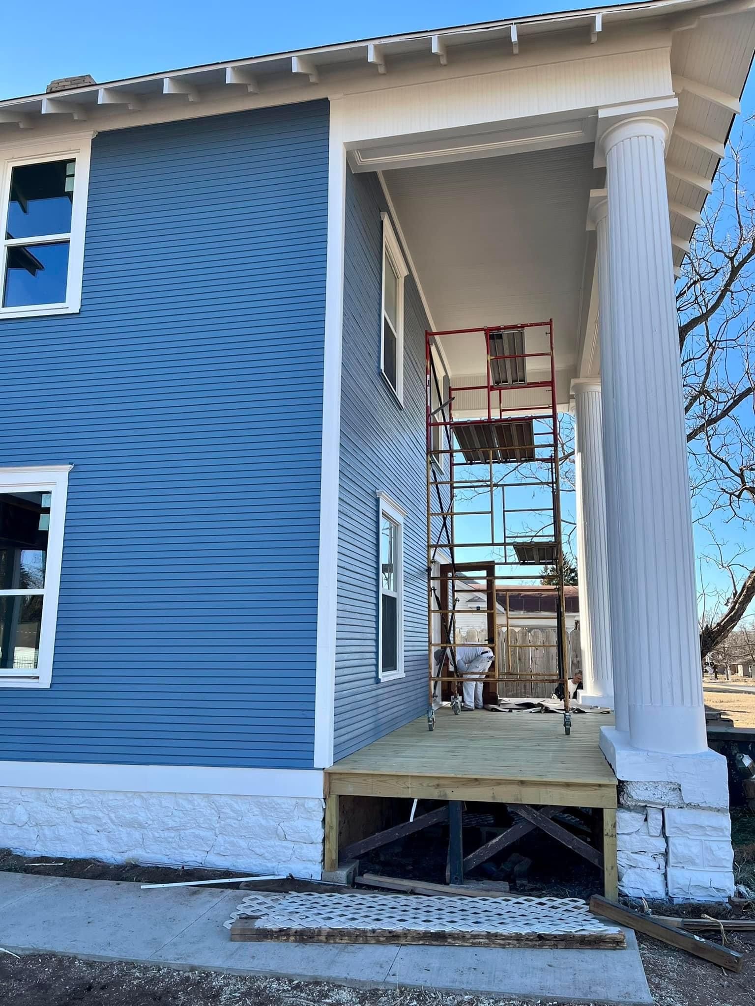 A blue and white house with a porch under construction.