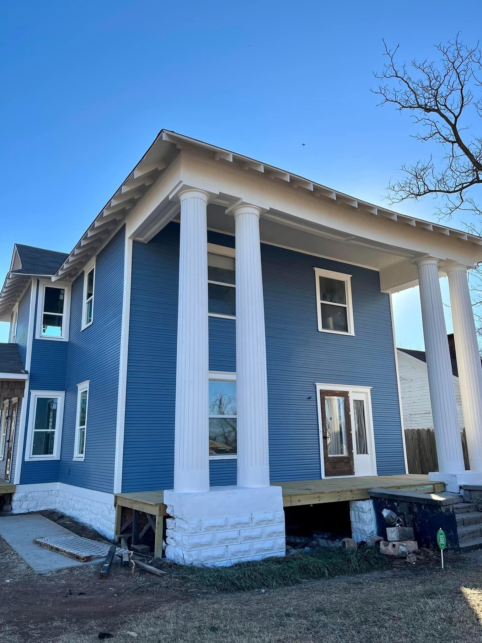 A blue house with white trim and columns is being built.