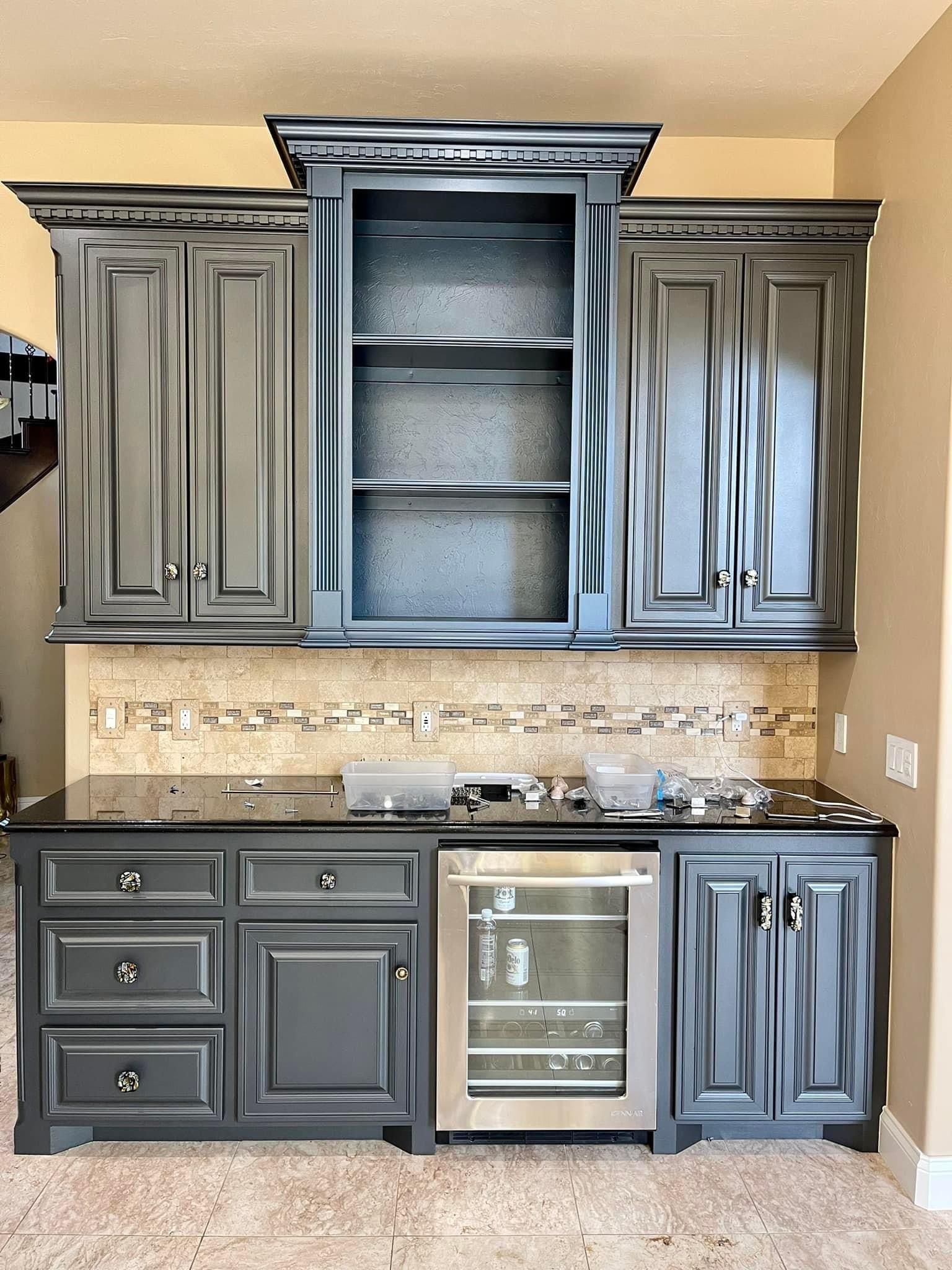 A kitchen with black cabinets and a stainless steel refrigerator.