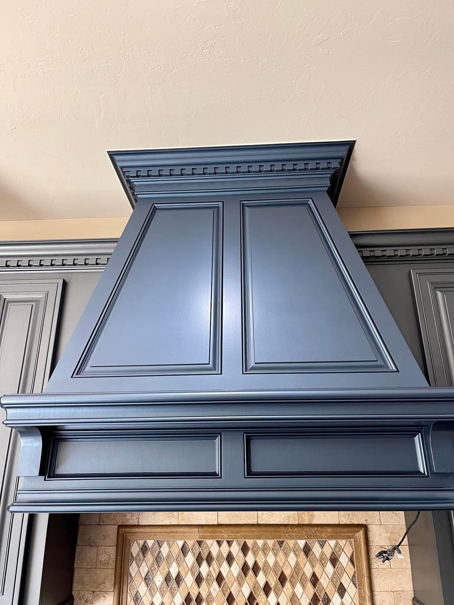A kitchen hood is hanging from the ceiling above a fireplace.