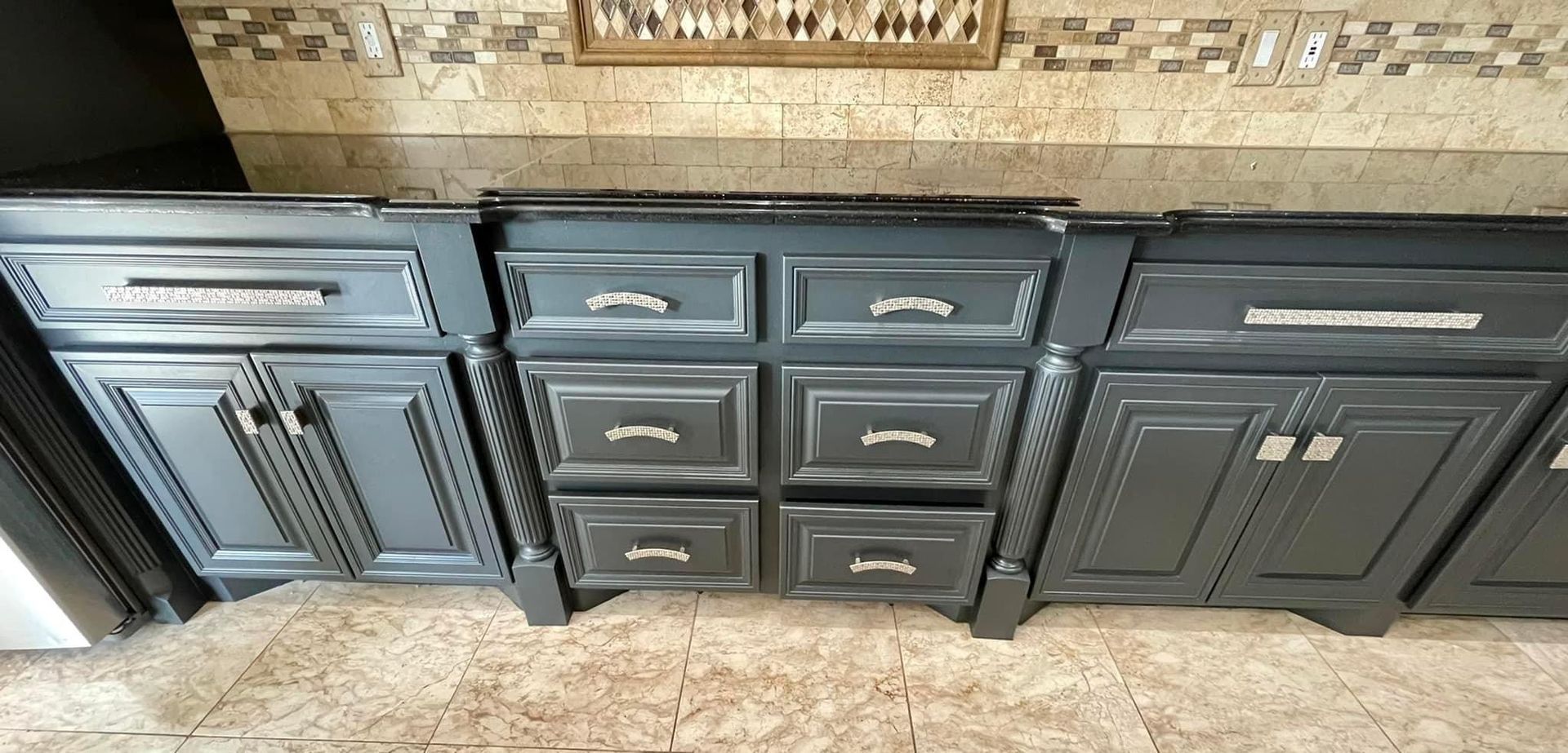 A kitchen with black cabinets and drawers and a tiled floor.