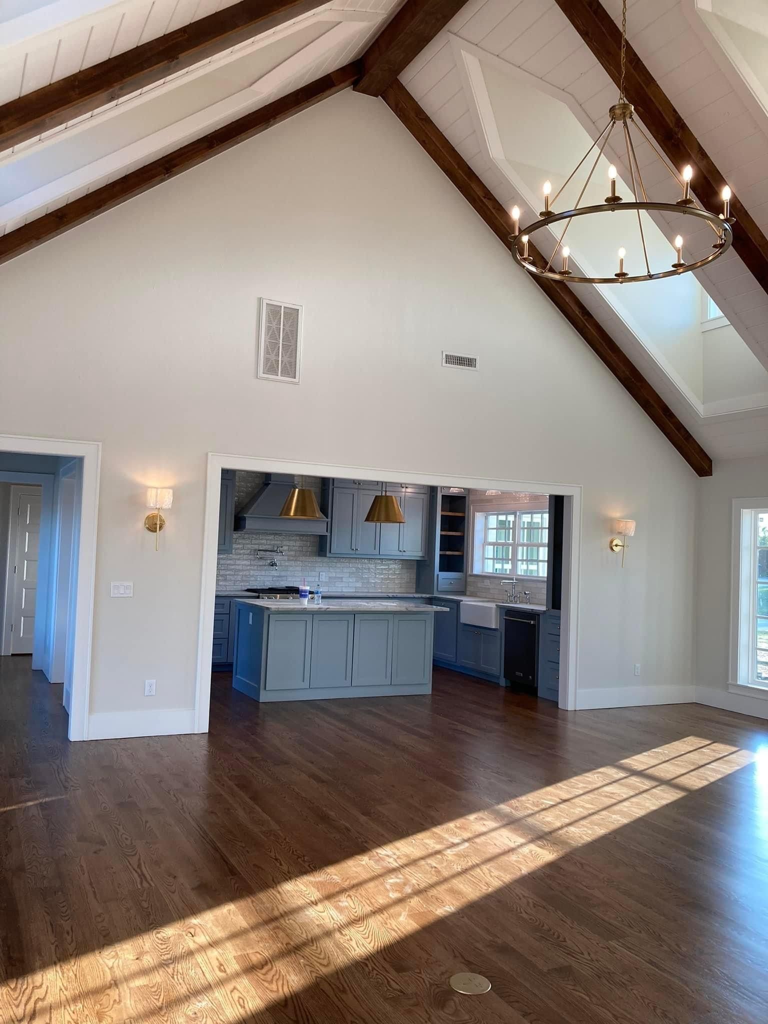 A large empty room with a kitchen and a chandelier hanging from the ceiling.