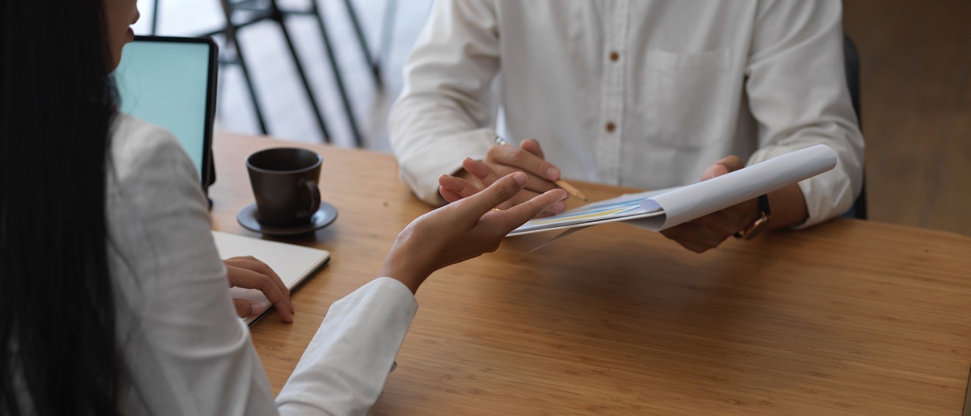 Business meeting with hands clasped, papers, laptop, and calculator on a wooden table.