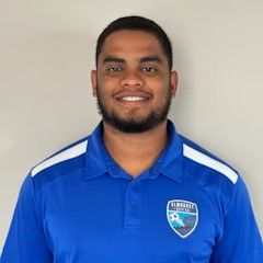 A man with a beard is wearing a blue polo shirt and smiling.