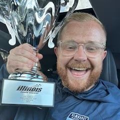 A man is holding a trophy in a car and smiling.
