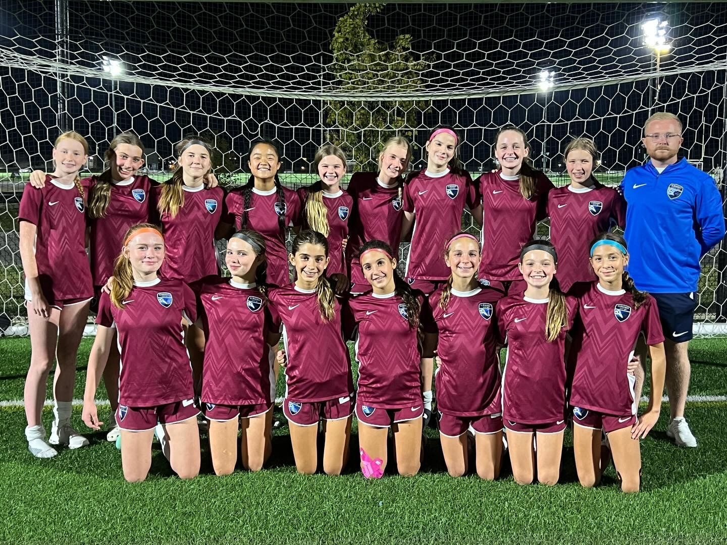 A group of young girls are posing for a picture on a soccer field.