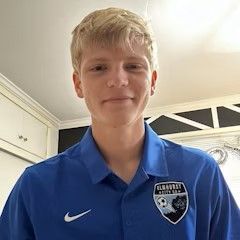 A young man wearing a blue nike shirt is standing in a kitchen.