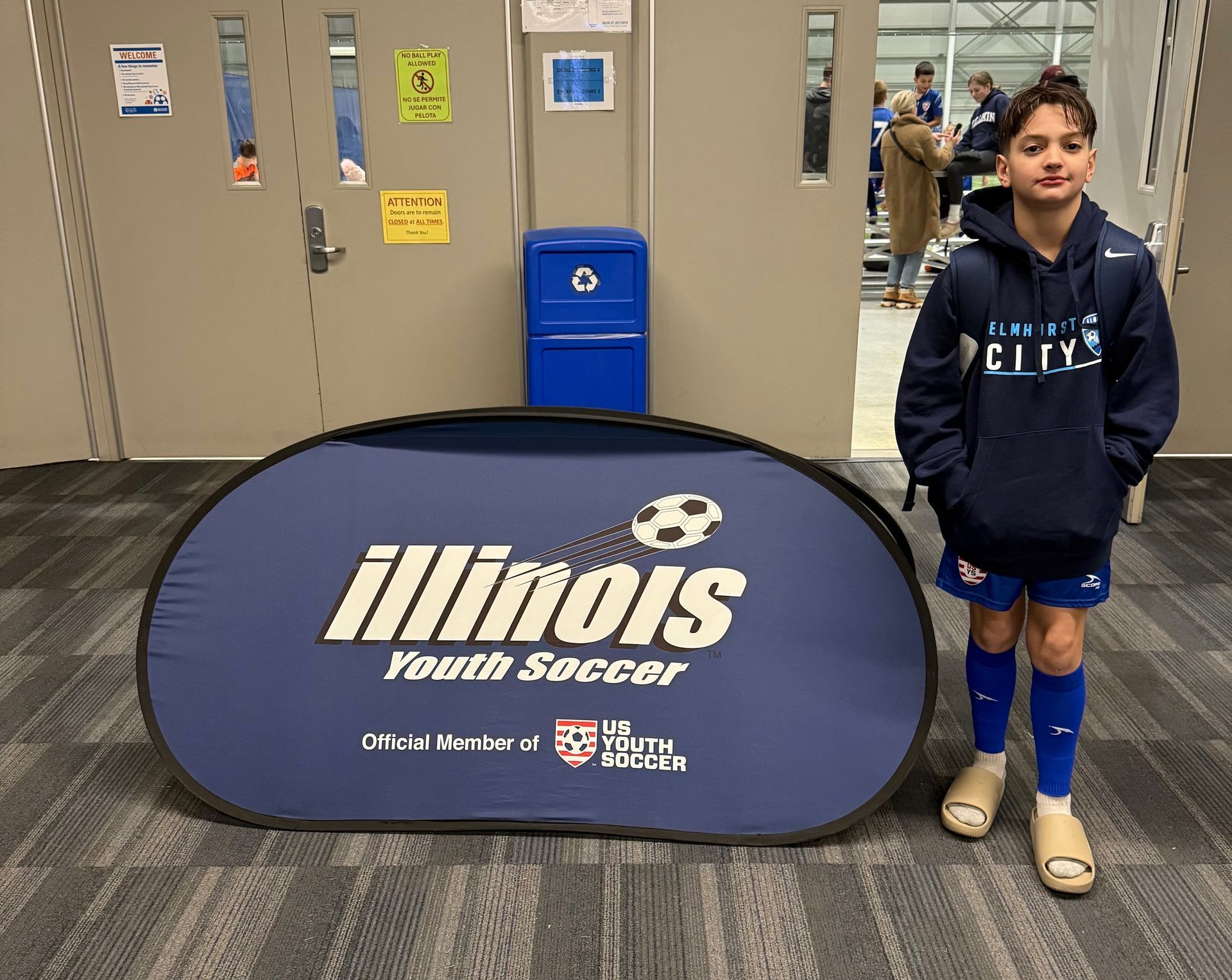 A young boy stands in front of an illinois youth soccer sign