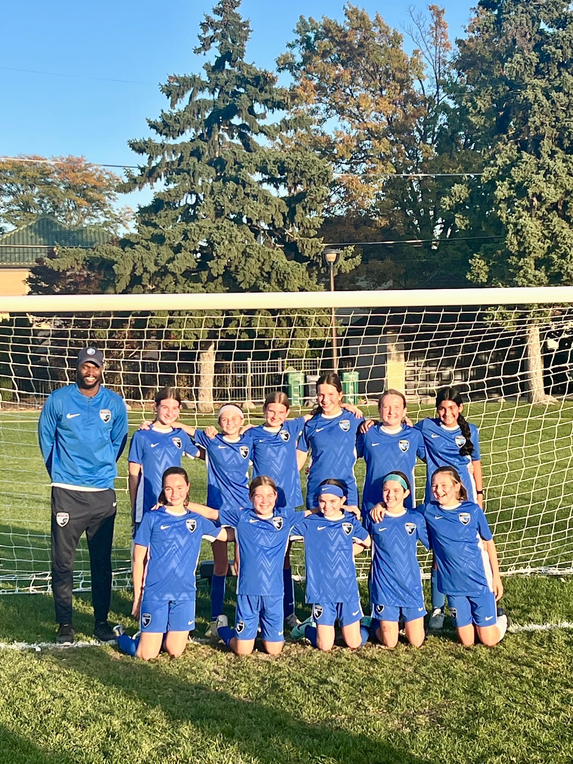 A group of young girls are posing for a picture on a soccer field.