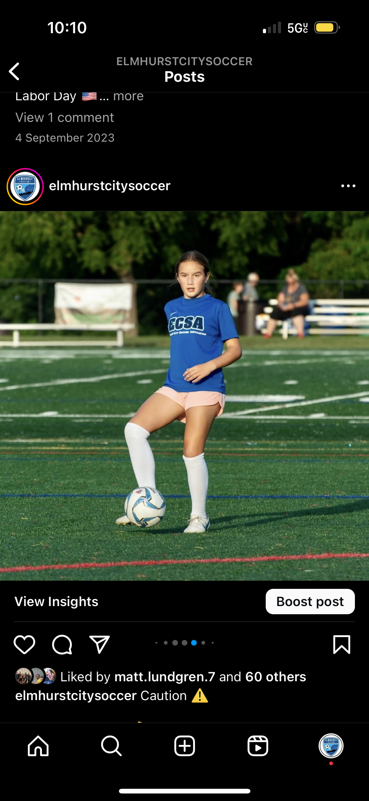 A girl in a blue shirt is kicking a soccer ball on a field.