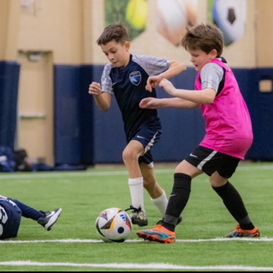 Two young boys are playing soccer and one is wearing a pink shirt