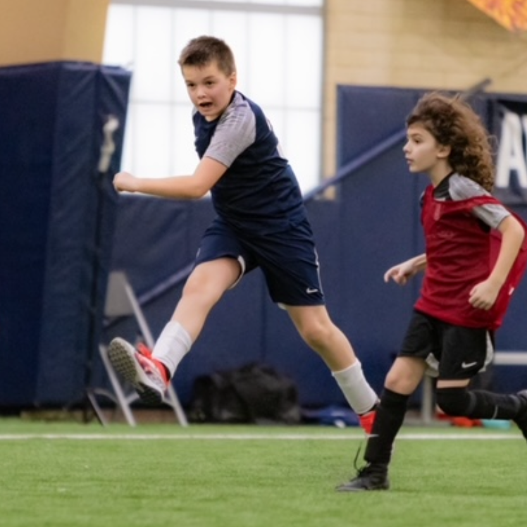 Two young boys are playing soccer and one is wearing a red shirt with the letter a on it
