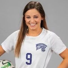 A woman in a white shirt with the number 9 on it is holding a soccer ball.