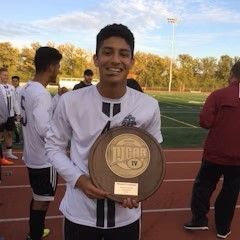 A young man is holding a trophy on a soccer field.