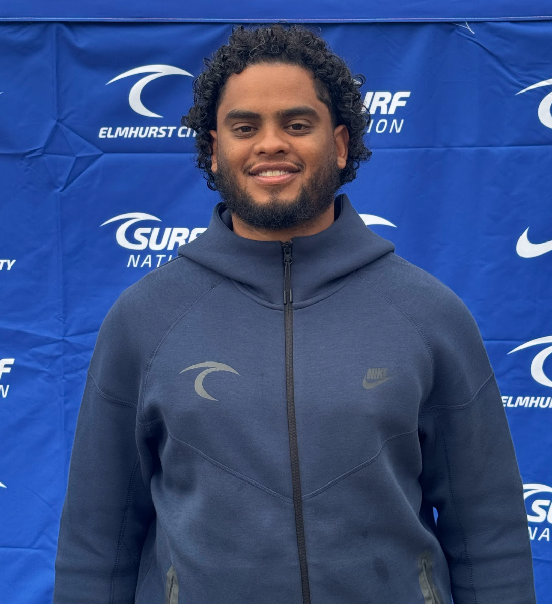 A man with a beard is wearing a blue polo shirt and smiling.