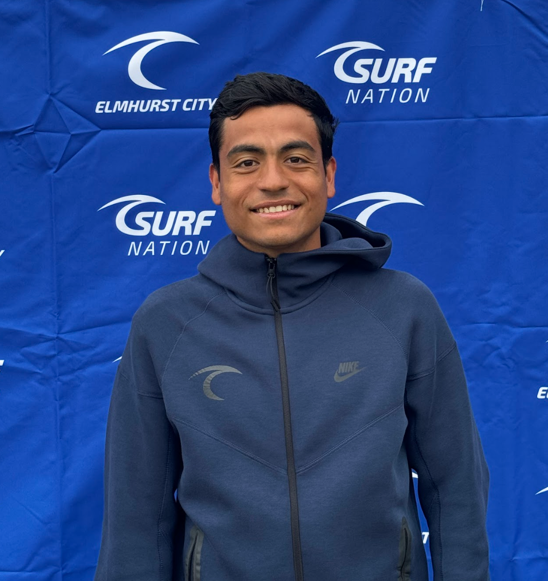 A man in a blue shirt is smiling in front of a soccer goal.