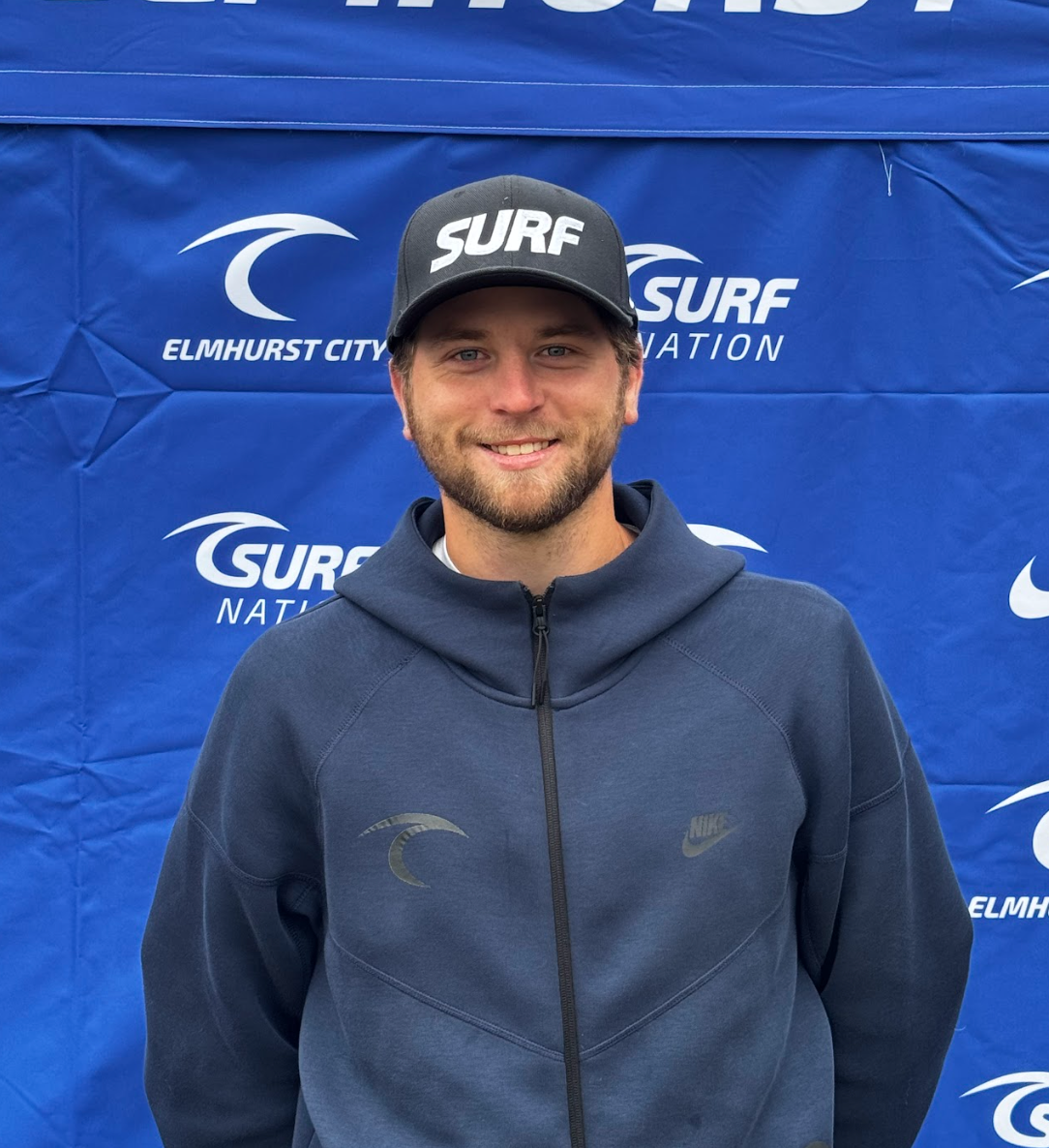 A young man with a beard is smiling for the camera while wearing a white shirt.