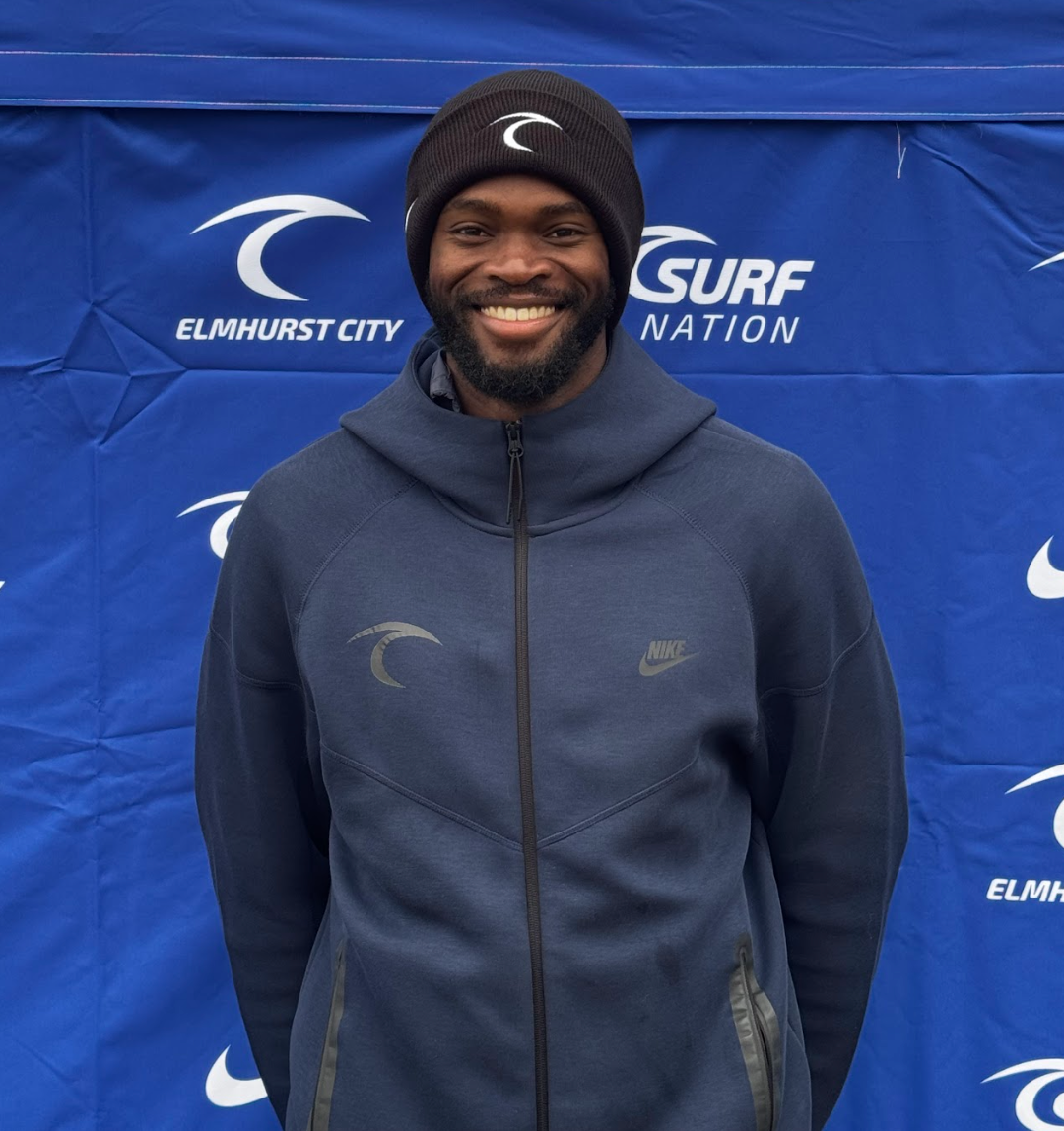 A man with a beard is wearing a blue shirt and smiling.