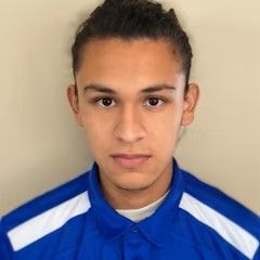 A young man wearing a blue and white shirt is looking at the camera.