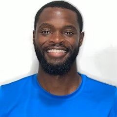 A man with a beard is wearing a blue shirt and smiling.