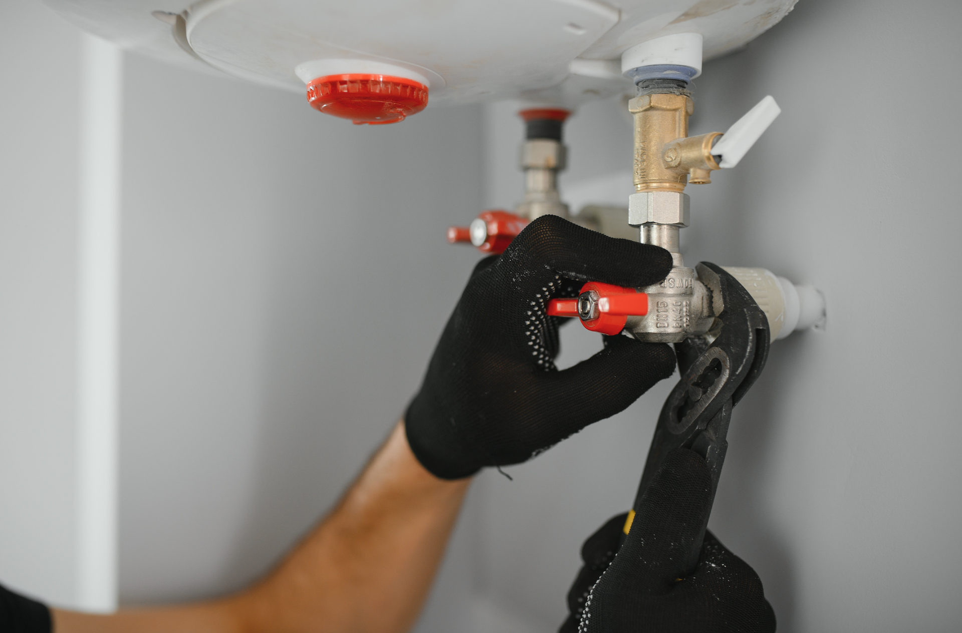 A person is fixing a water heater with a wrench.