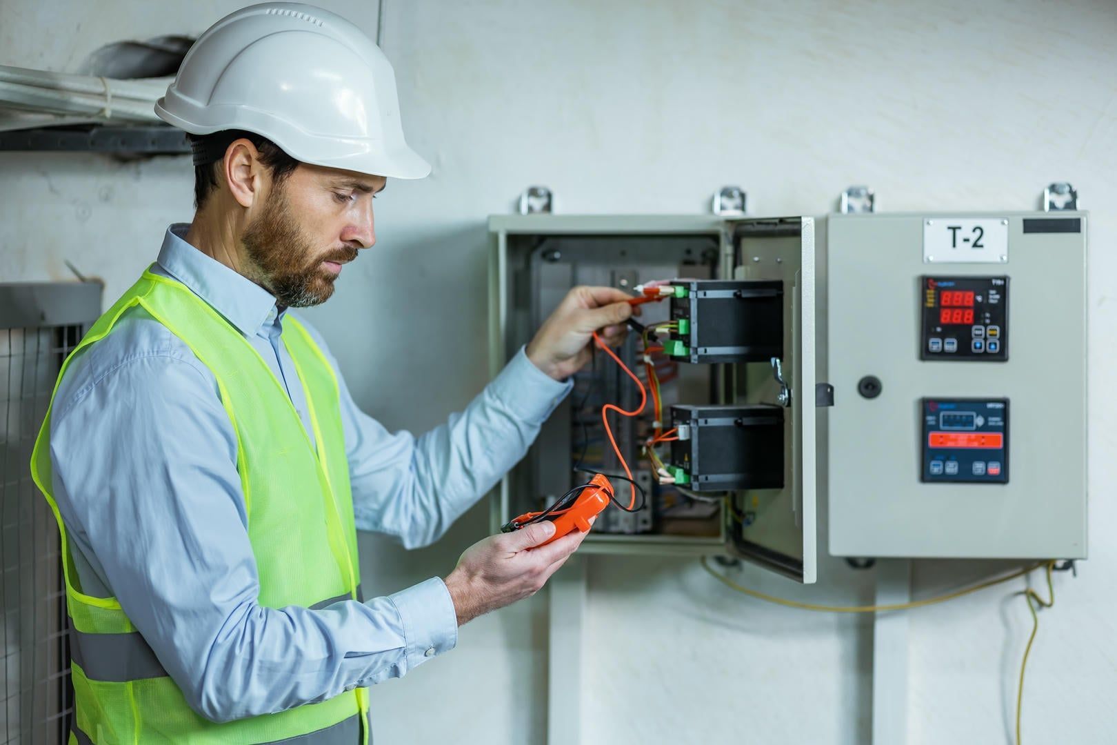 A man in a hard hat and safety vest is working on an electrical box.
