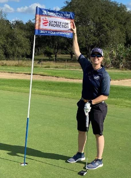 Owner Suzanne Saults holds flag on golf course for sponsorship of tournament 