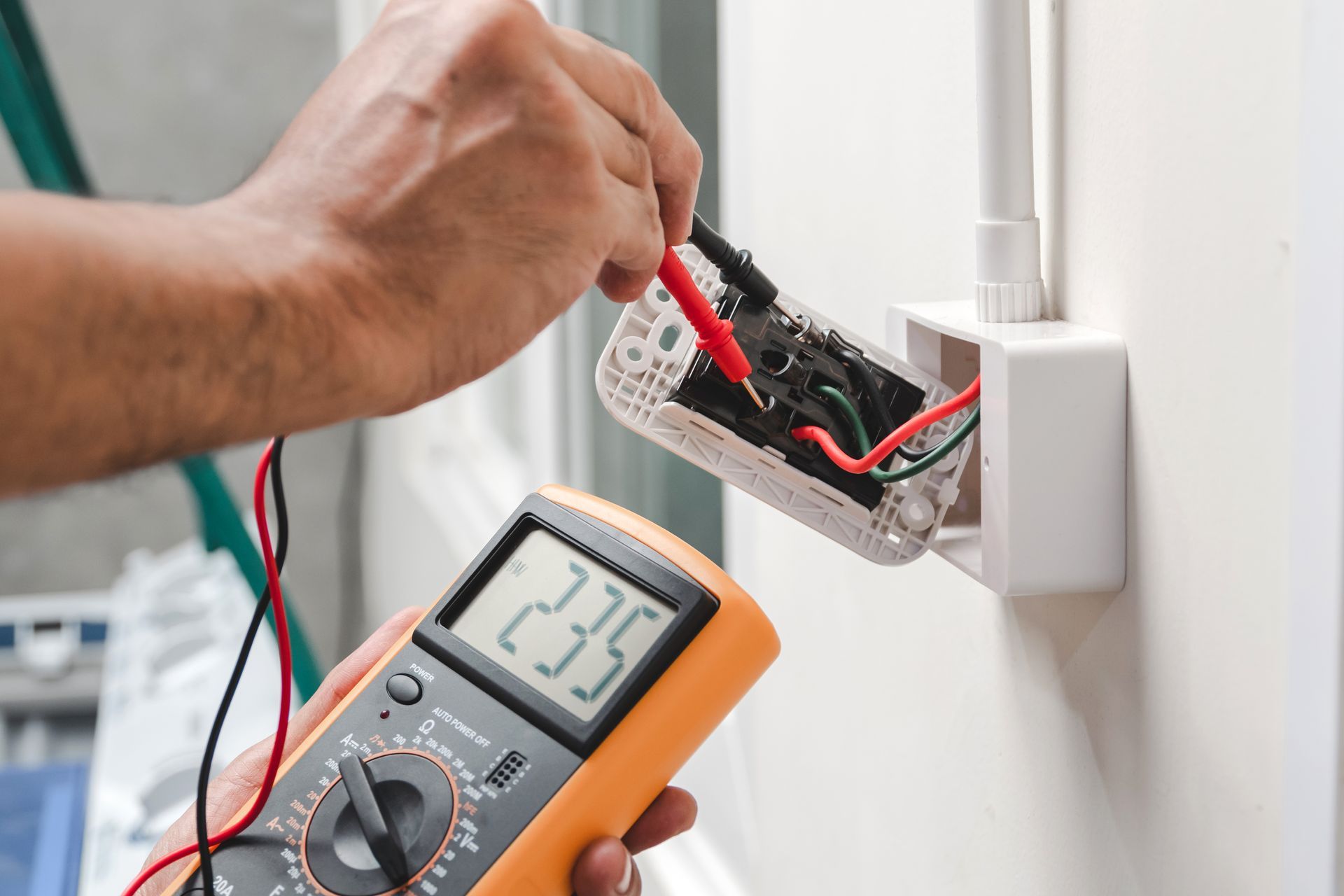 A person is using a multimeter to test an electrical outlet.