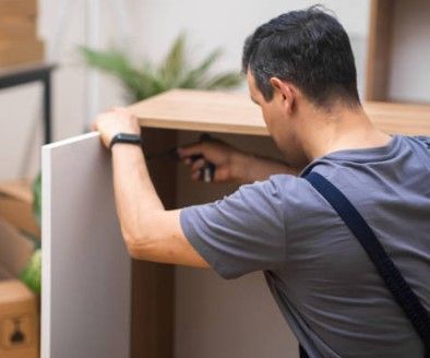 Mann im grauen Hemd montiert mit einem Werkzeug Möbel im Haus.