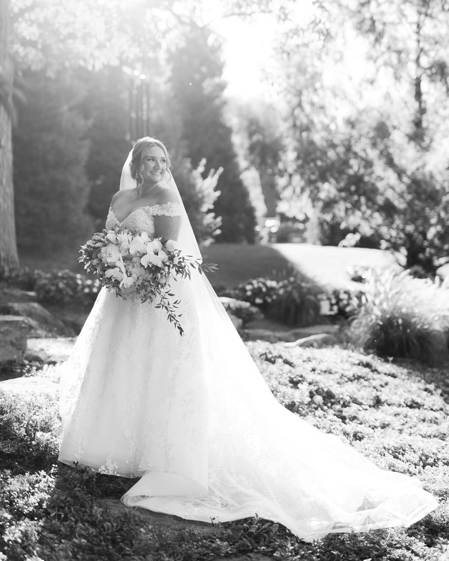 A black and white photo of a bride in a wedding dress holding a bouquet of flowers.