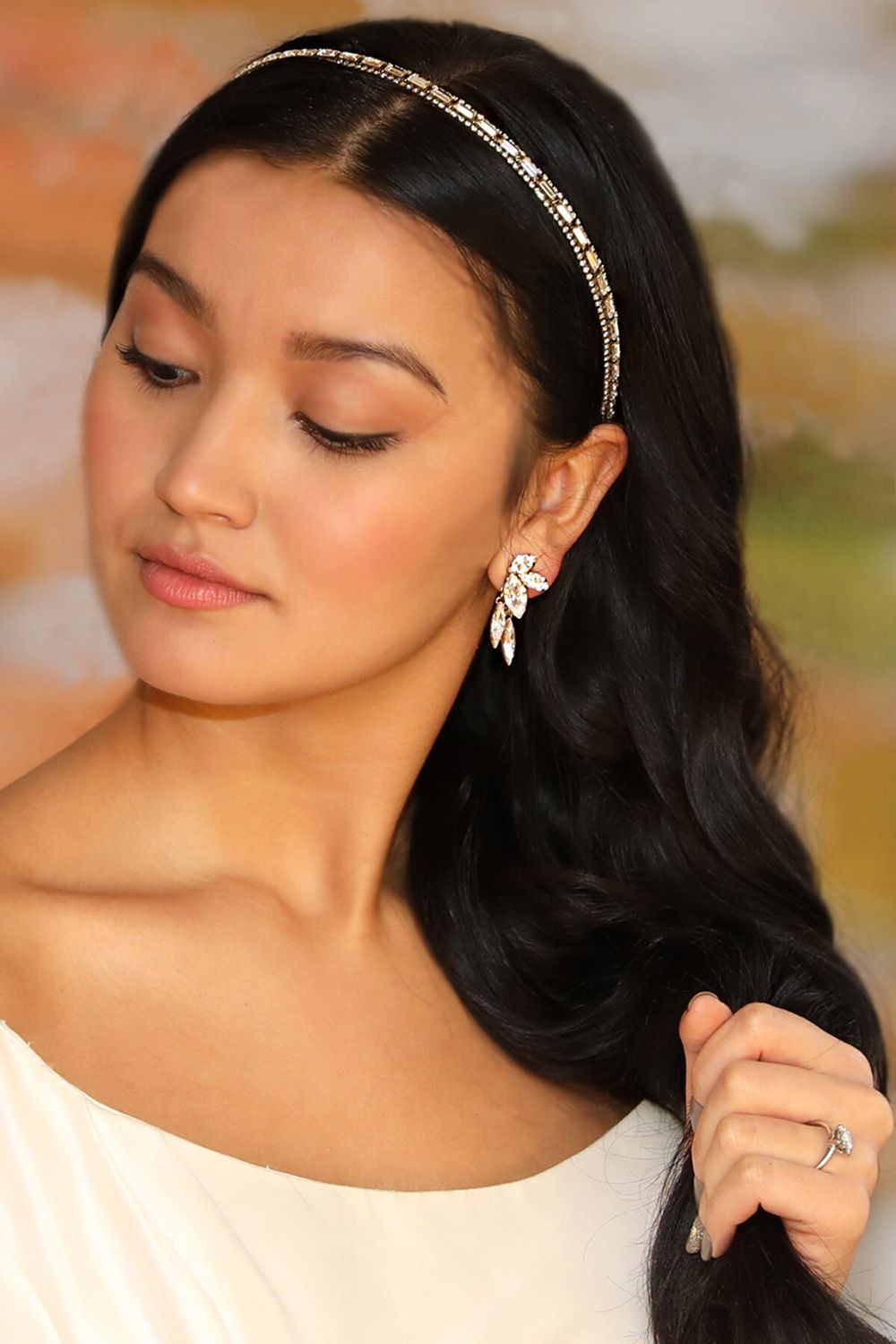A woman wearing a headband and earrings is holding her hair.
