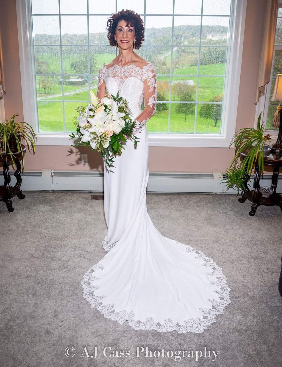 A woman in a wedding dress is standing in front of a window holding a bouquet of flowers.