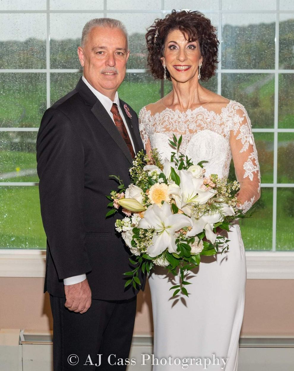 A bride and groom pose for a picture in front of a window