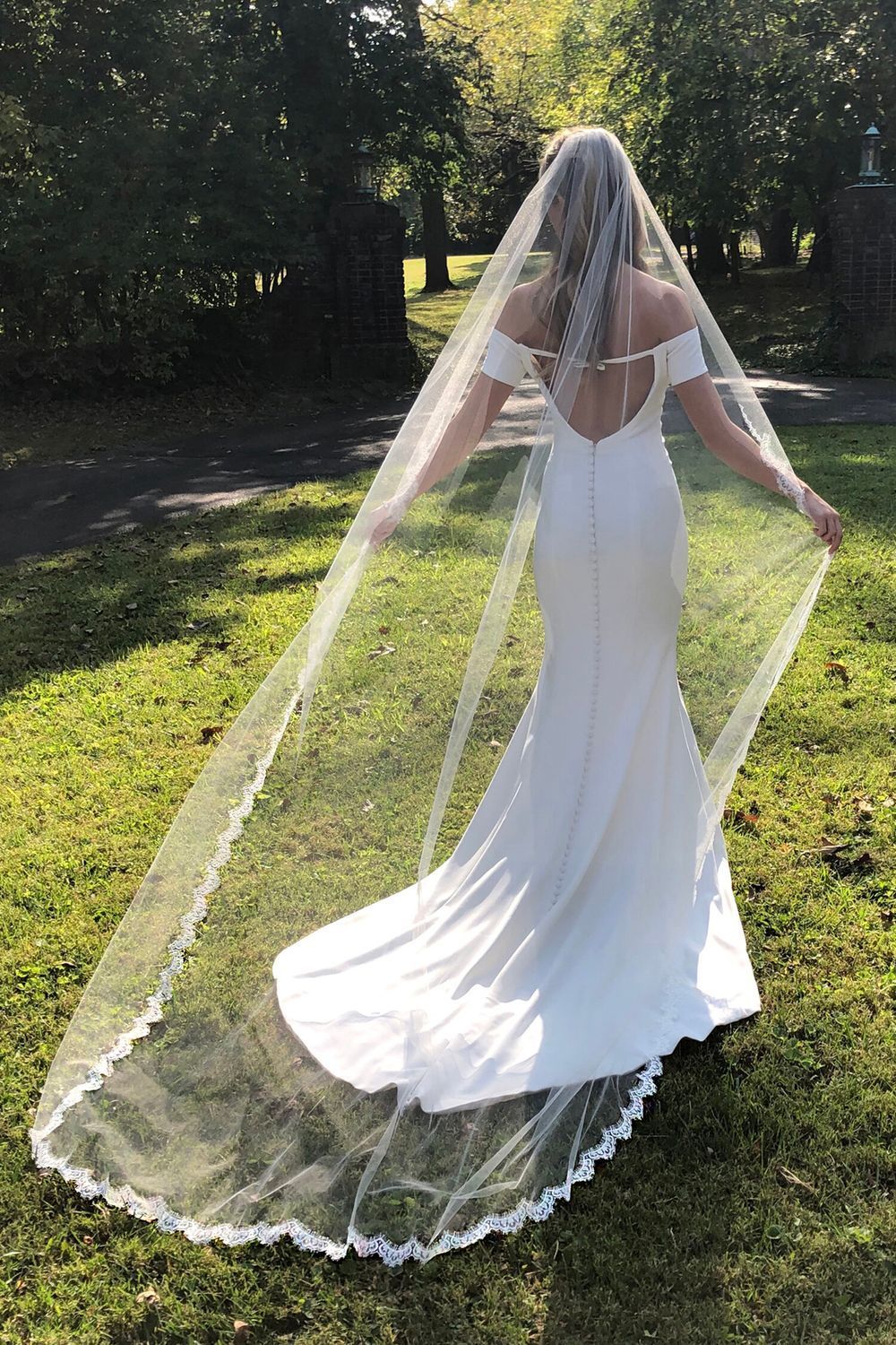 A woman in a wedding dress and veil is standing in the grass.
